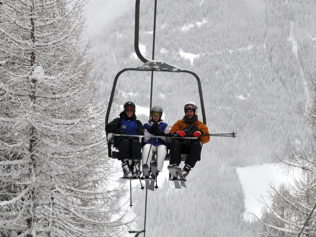 Zwei Personen fahren im Sessellift durch den verschneiten Wald.